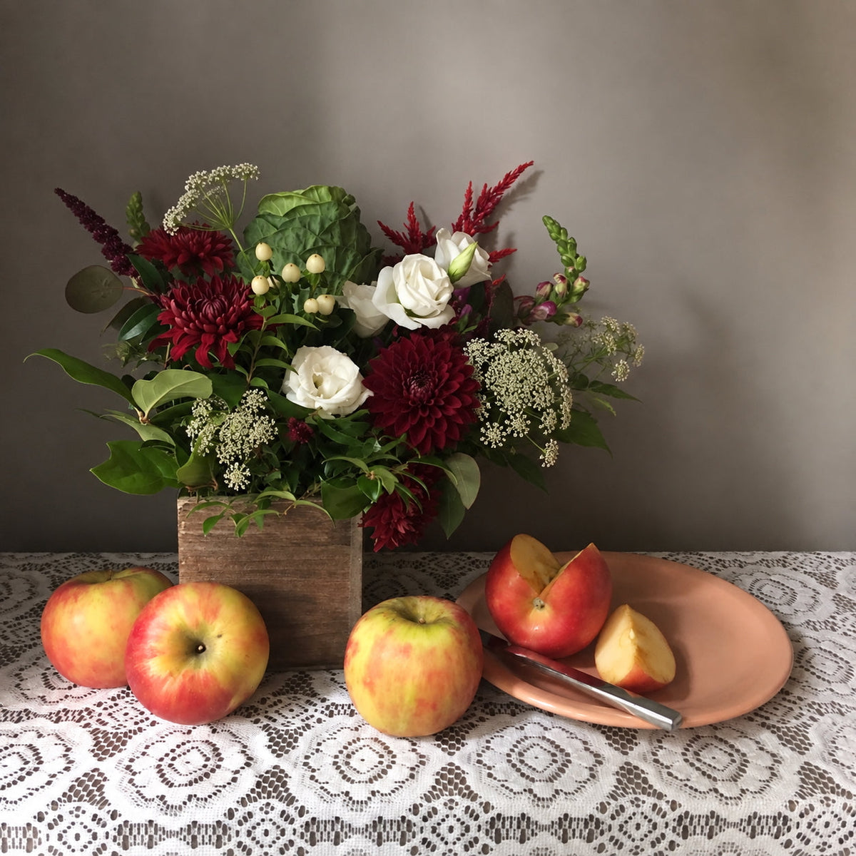 Deep red floral arrangement from Flowers for Dreams in a wooden box next to fresh apples for Rosh Hashanah.