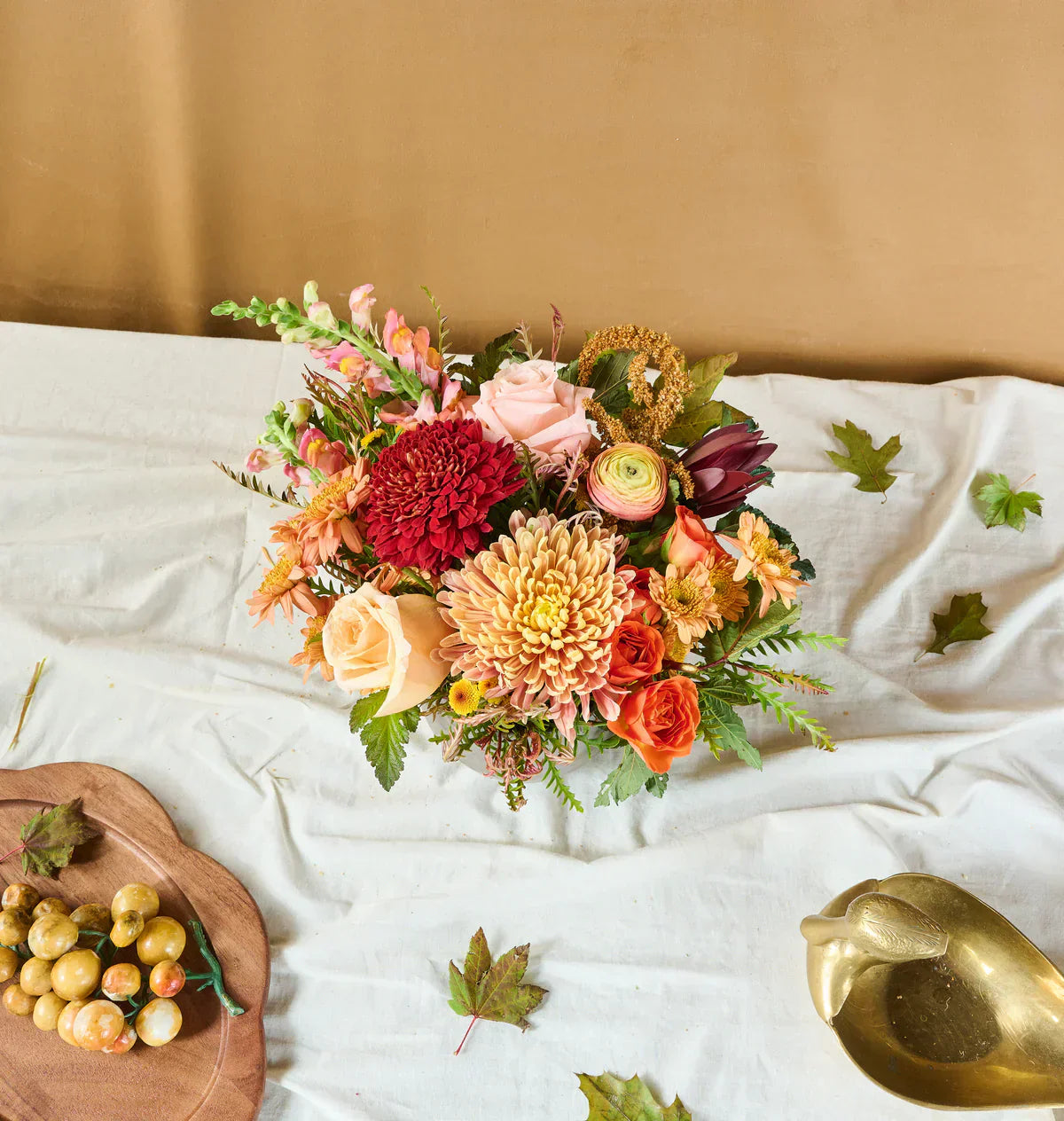 Fall bouquet from Flowers for Dreams with orange, peach, and red blooms wrapped in burlap on a plaid cloth.