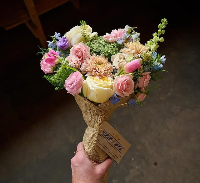 Hand holding a rustic wrapped bouquet of pastel flowers, ready for gifting from Flowers for Dreams.