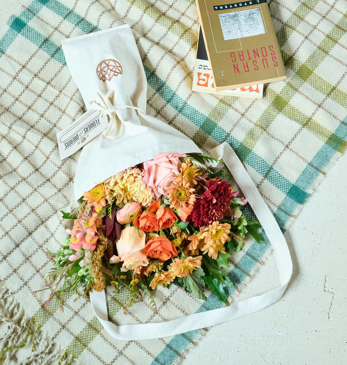 A vibrant Flowers for Dreams bouquet of peach, orange, and deep red blooms wrapped in a white sleeve on plaid cloth.