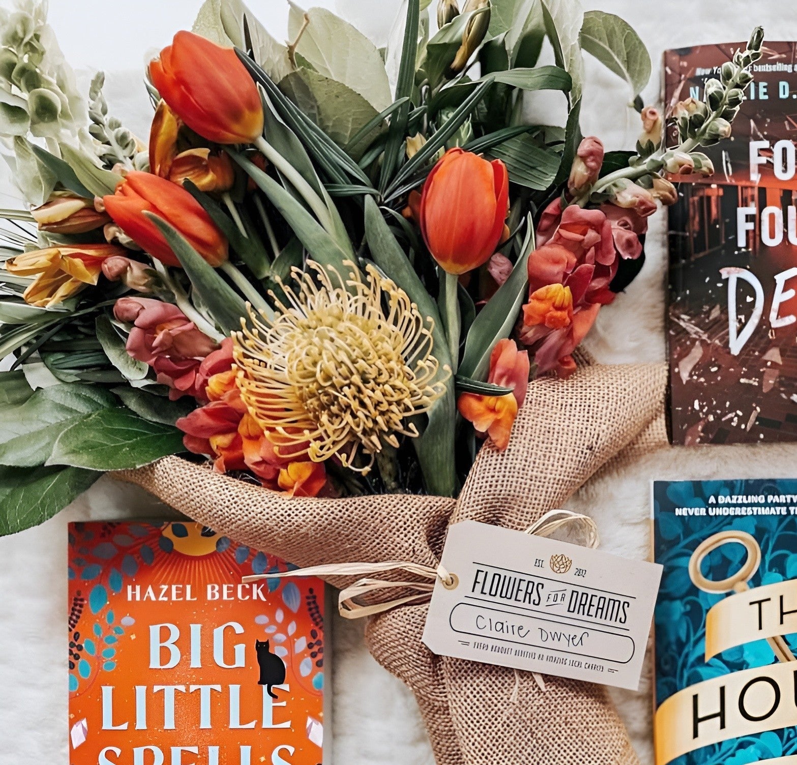 Vibrant orange tulips and a yellow flower centerpiece from Flower for Dreams in a burlap-wrapped bouquet with books.