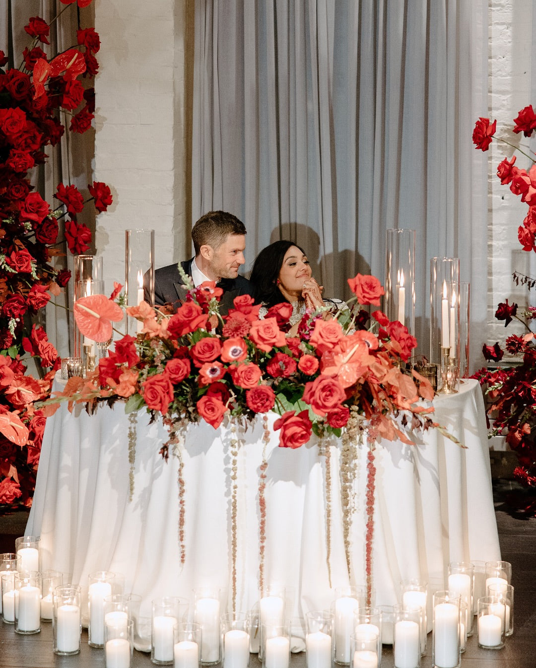Close-up of a Flowers for Dreams table draped with red and pink floral garlands against a dark background.