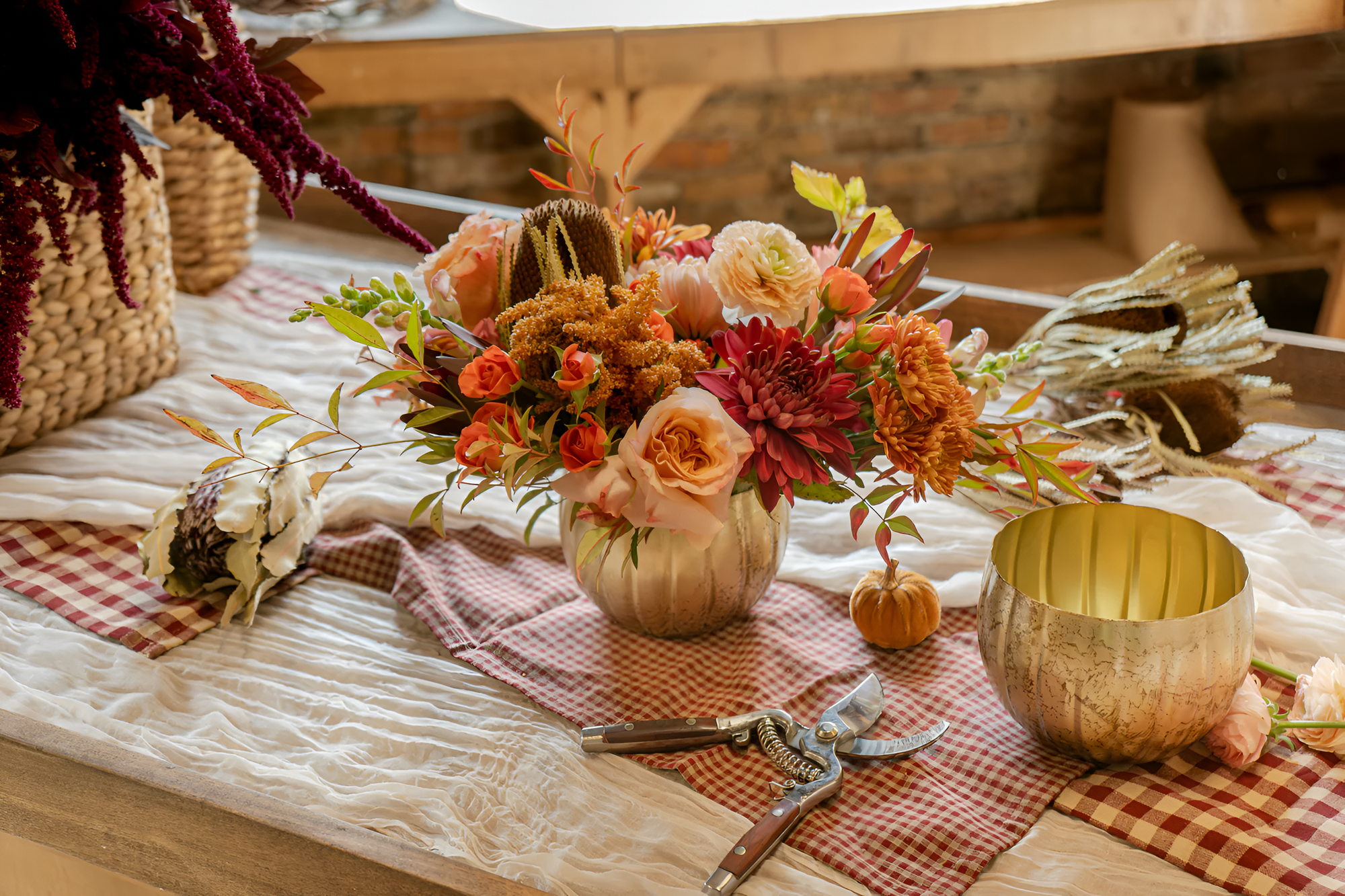 Warm fall bouquet with roses and mums arranged by Flowers for Dreams in a textured gold vase on a table.