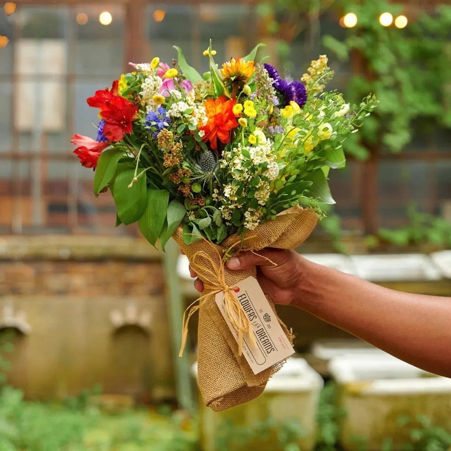 Vibrant wildflower bouquet wrapped in burlap, held by hand from Flowers for Dreams.