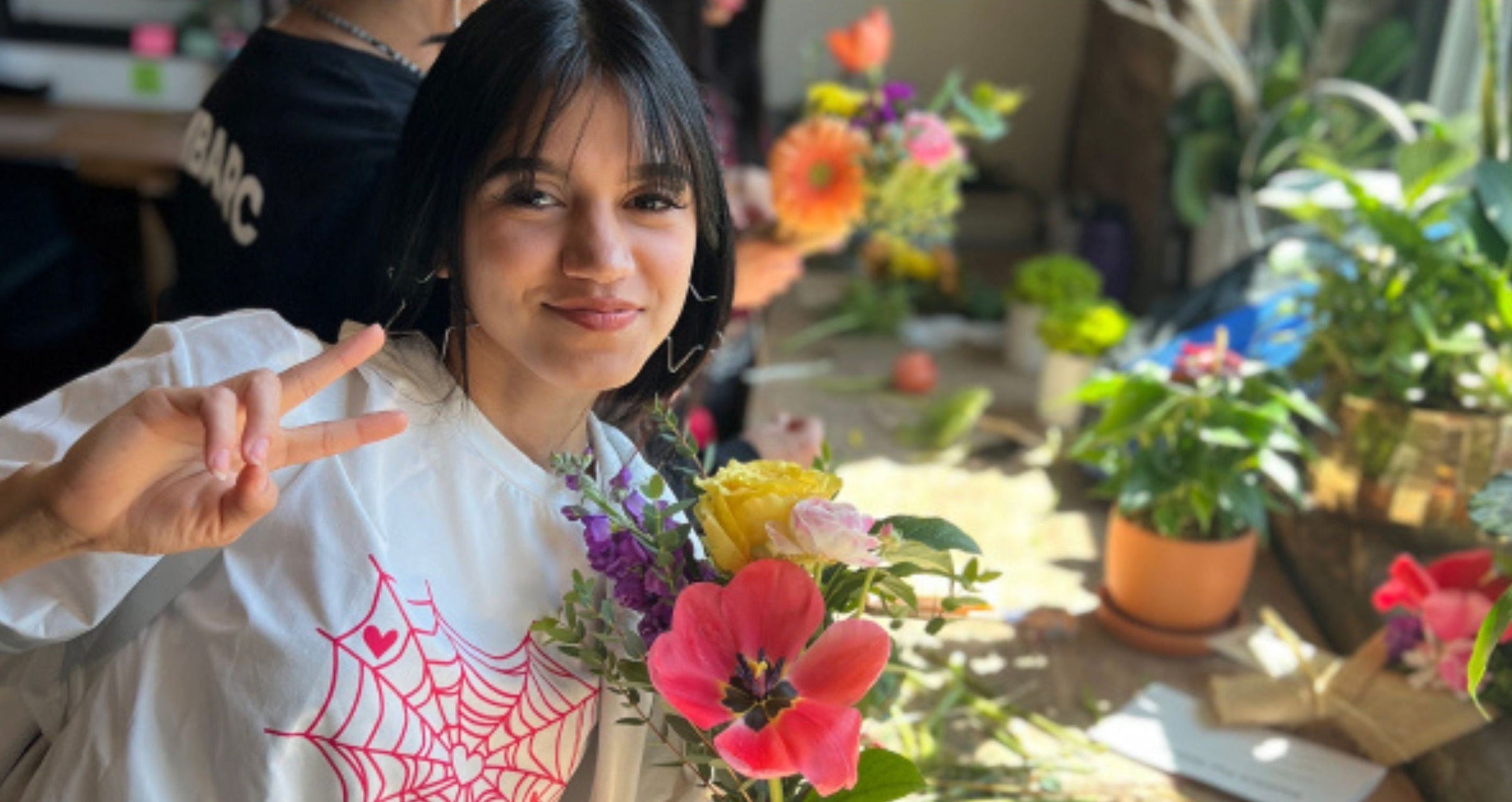  A young woman smiling and making a peace sign while holding a colorful bouquet from Flowers for Dreams.