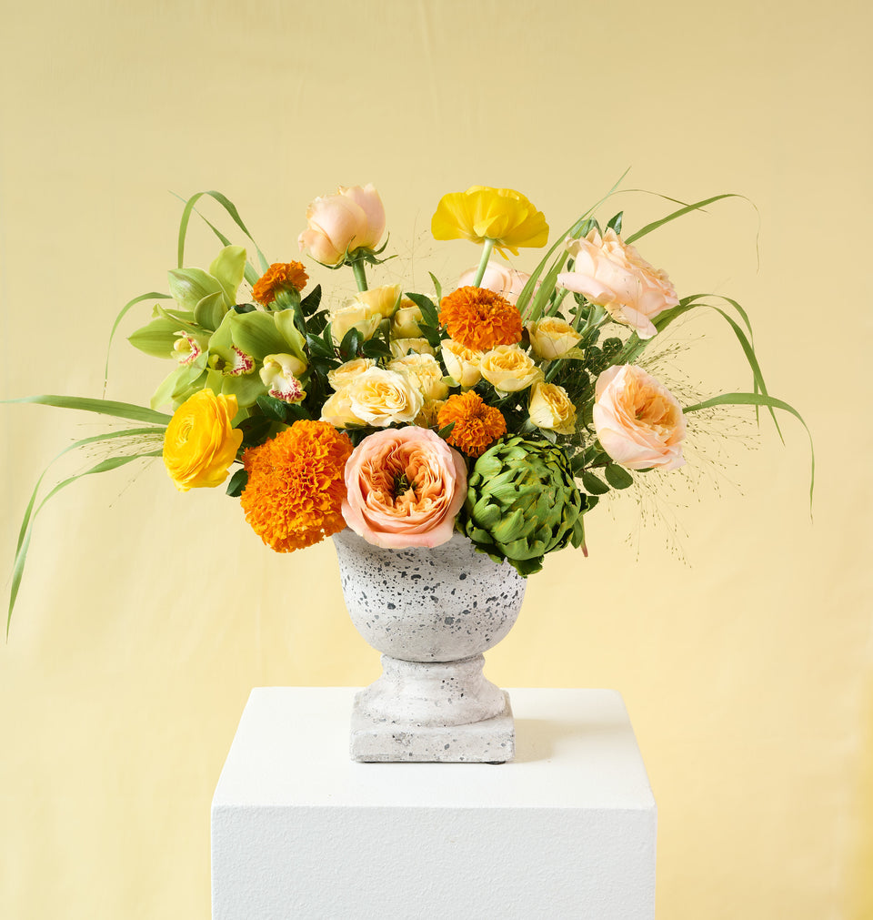 Clementine bouquet in a compote vase with vibrant warm-toned flowers