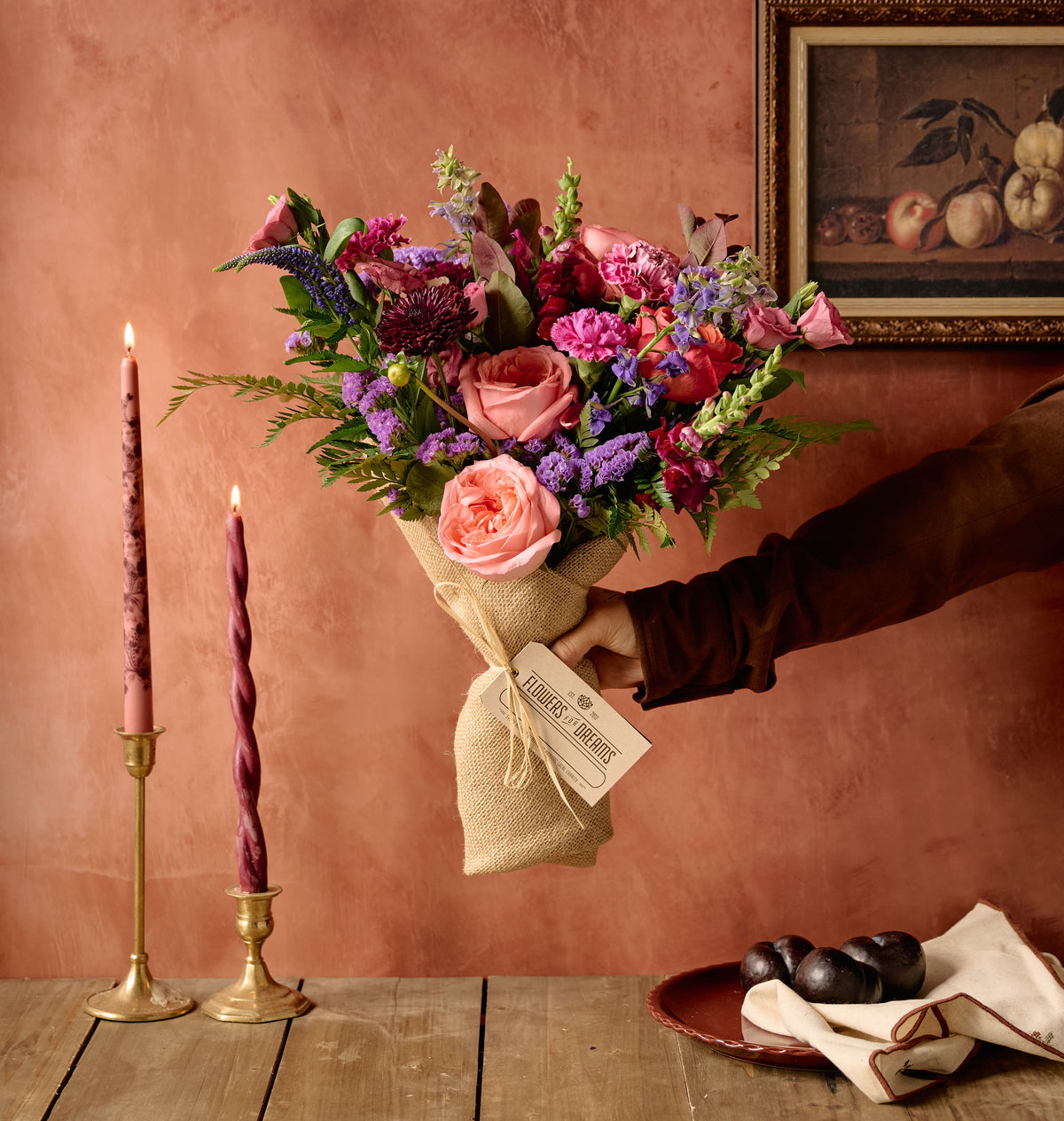 Berry floral arrangement of plum lisianthus, dusty pink roses, and hypericum berries in a stone-textured ceramic vessel, moody background
