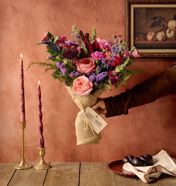 Berry floral arrangement of plum lisianthus, dusty pink roses, and hypericum berries in a stone-textured ceramic vessel, moody background