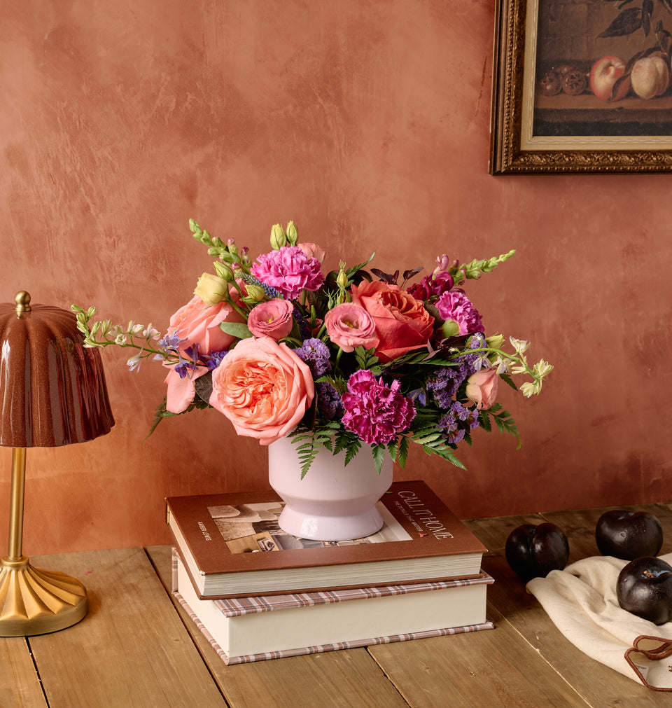Berry floral arrangement of deep purple lisianthus, burgundy dahlias, pink roses, and mixed berries in a white ceramic vase on dark moody background