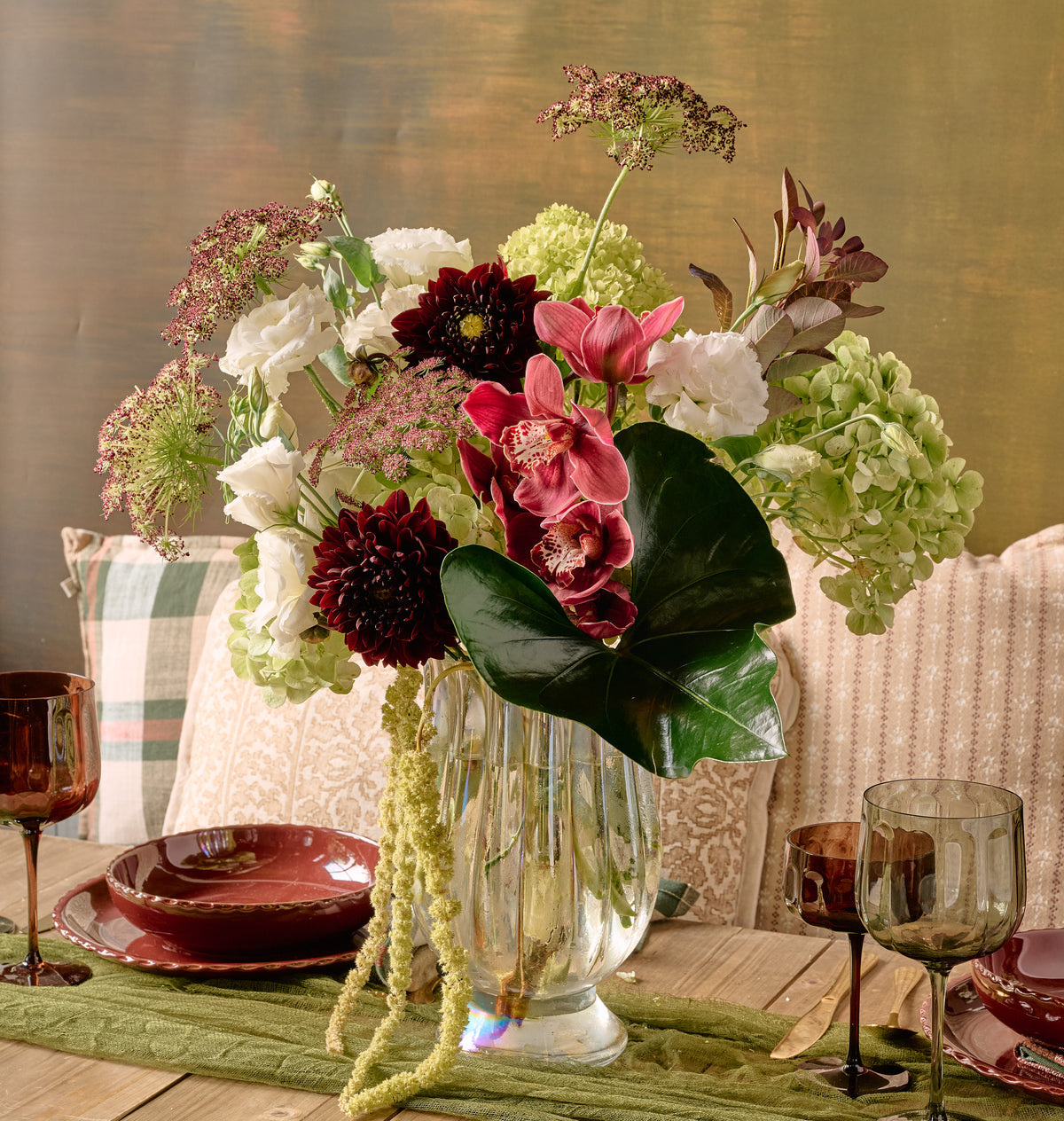 Bordeaux floral arrangement of deep burgundy dahlias, dark red roses, chocolate cosmos, and amaranth in a crystal vase on dark dramatic background