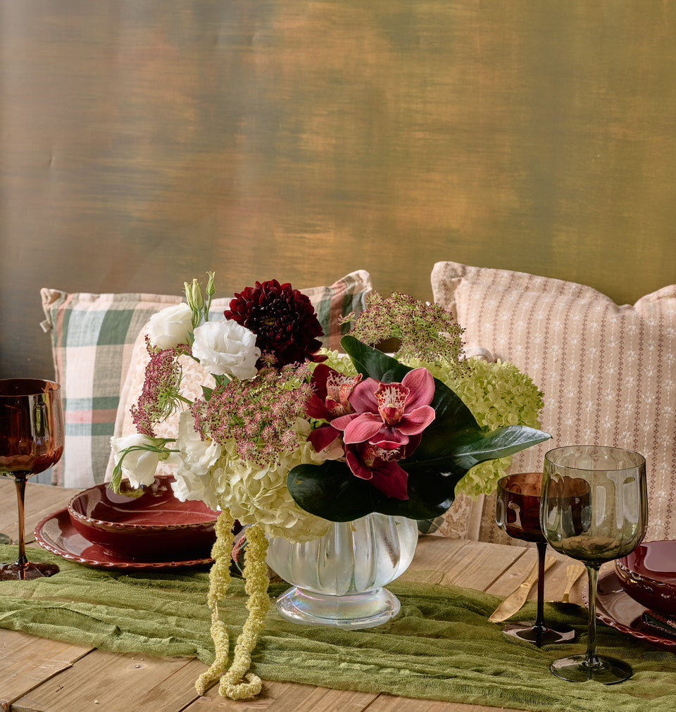 Bordeaux grand floral arrangement of deep red roses, burgundy dahlias, chocolate cosmos, and dark amaranth in a large crystal vase, dramatic dark background