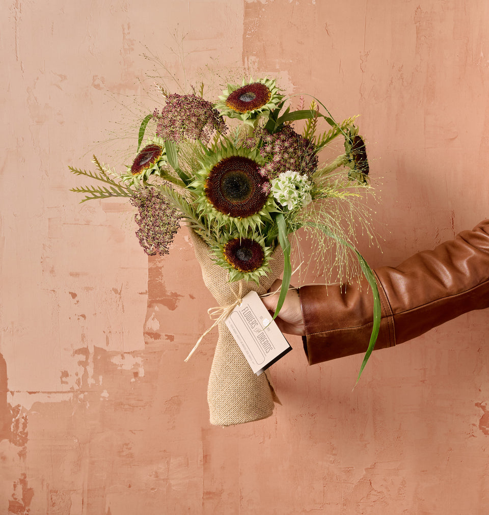 Muse floral bouquet of blush garden roses, coral ranunculus, and lisianthus wrapped in white ribbon on soft neutral background