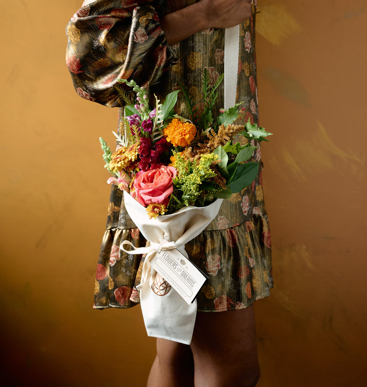 Autumn floral arrangement of pink roses, orange marigolds, chrysanthemums, and amaranth in a clear mason jar on hay bale with gourds, amber background